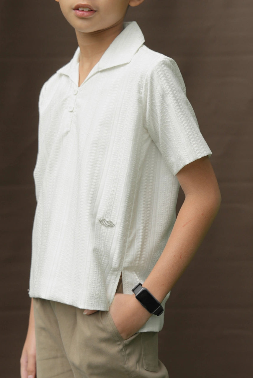 Child wearing a white textured shirt by Mistyvori and beige pants against a brown background
