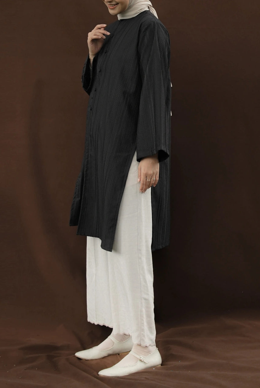 Person wearing a black tunic by Mistyvori over a white outfit on a brown background.
Seorang wanita mengenakan tunik hitam dari Mistyvori di atas pakaian putih dengan latar belakang cokelat.