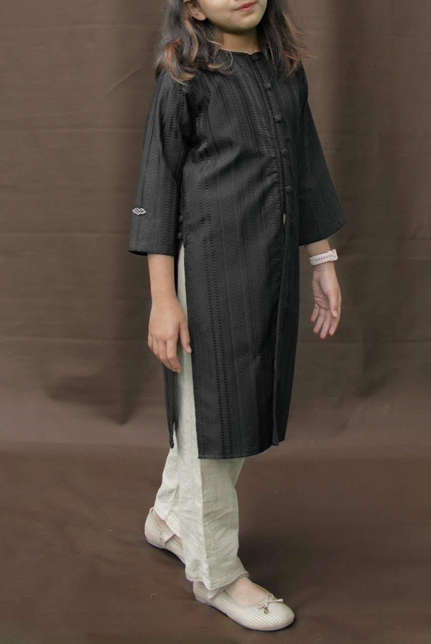 Child wearing a black tunic by Mistyvori with beige pants on a brown background.
Seorang anak mengenakan tunik hitam dari Mistyvori dengan celana krem di atas latar belakang cokelat.