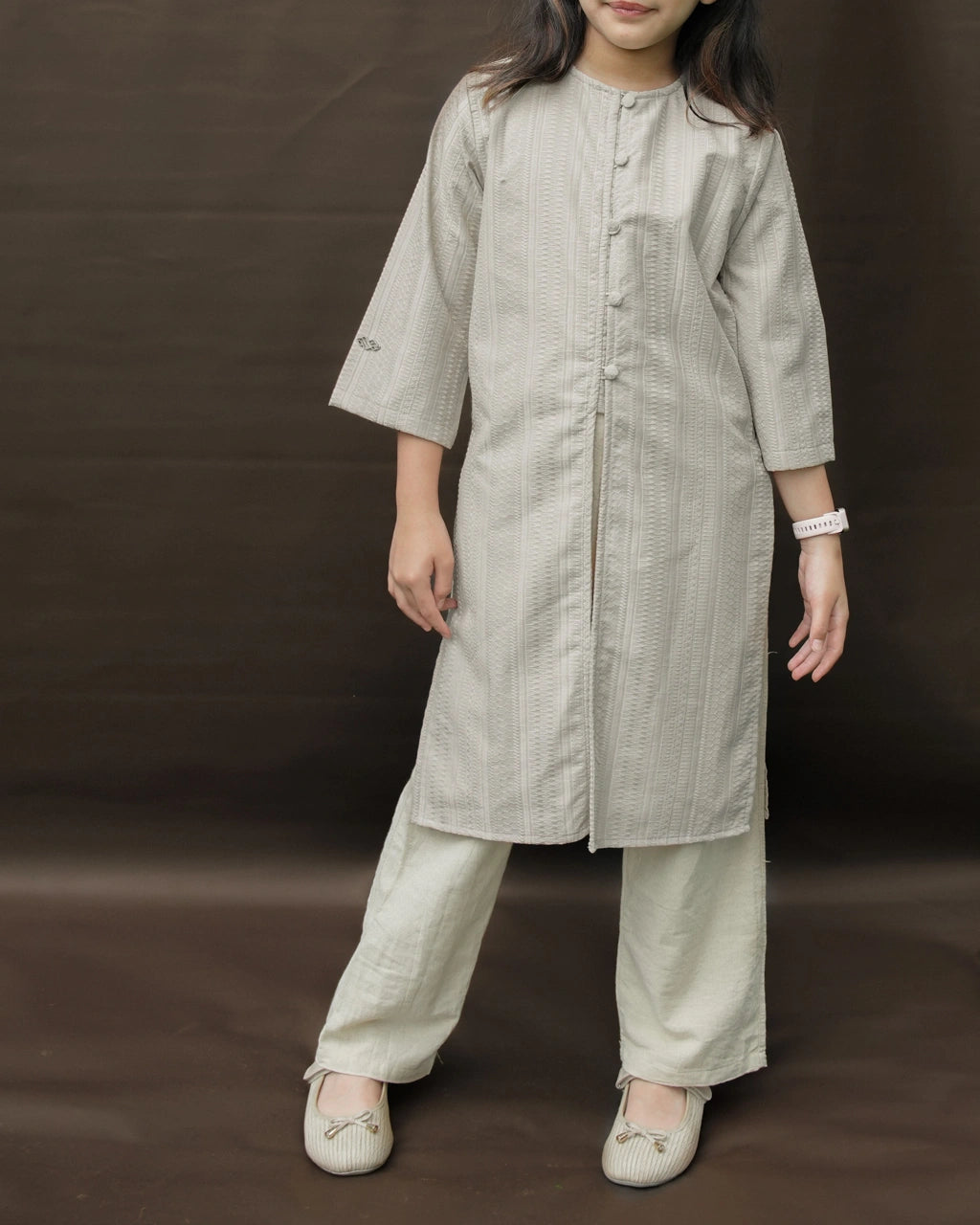 Child wearing a light gray tunic by Mistyvori with light gray pants on a brown background.
Seorang anak mengenakan tunik abu-abu muda dari Mistyvori dengan celana abu-abu muda di atas latar belakang cokelat.
