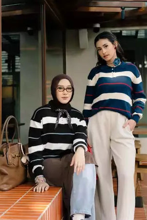 Two women standing outdoors, wearing a striped knit sweater by Haidee Orlin, with a handbag on a ledge.