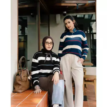 Two women standing outdoors, wearing a striped knit sweater by Haidee Orlin, with a handbag on a ledge.