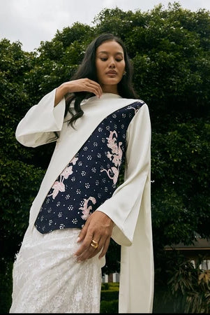 A woman wearing a traditional white blouse by Kartinis Label with asymmetrical batik design on the yoke, featuring floral patterns and bead details.