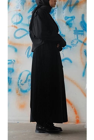 Person wearing a long black skirt from Rahawl standing against a colorful graffiti wall.