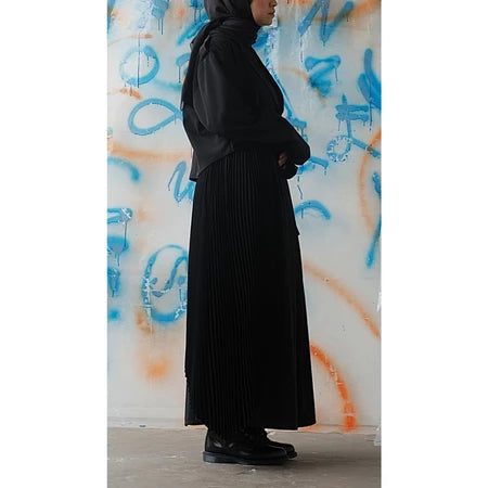 Person wearing a long black skirt from Rahawl standing against a colorful graffiti wall.