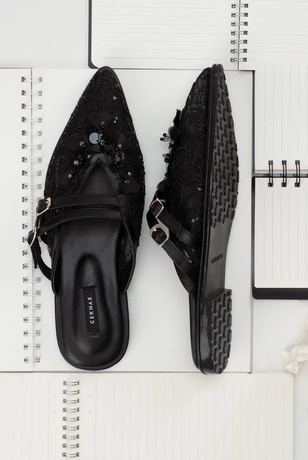 Black pointed-toe mules sandals by Cekhas on a white surface with a notebook