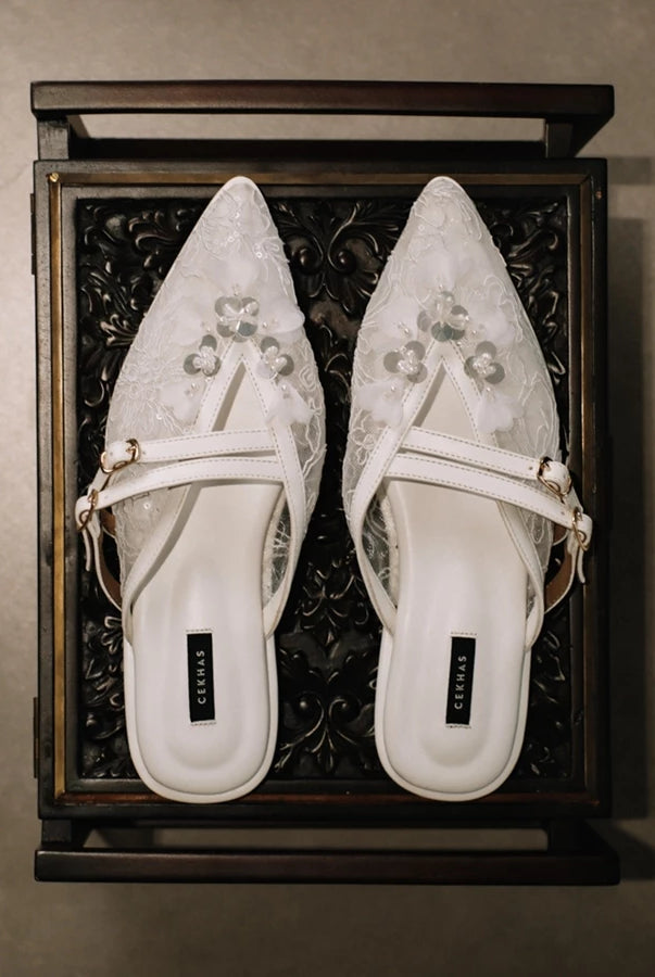Pair of white pointed-toe mules sandals by Cekhas with floral designs in a decorative wooden box.