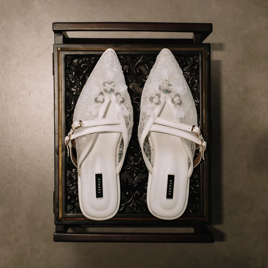 Pair of white pointed-toe mules sandals by Cekhas with floral designs in a decorative wooden box.