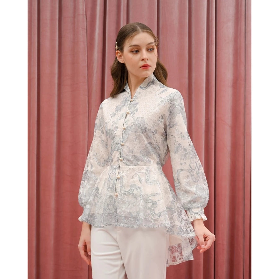 Woman wearing a floral blue blouse by Kasa Heritage and white pants against a pink curtain background