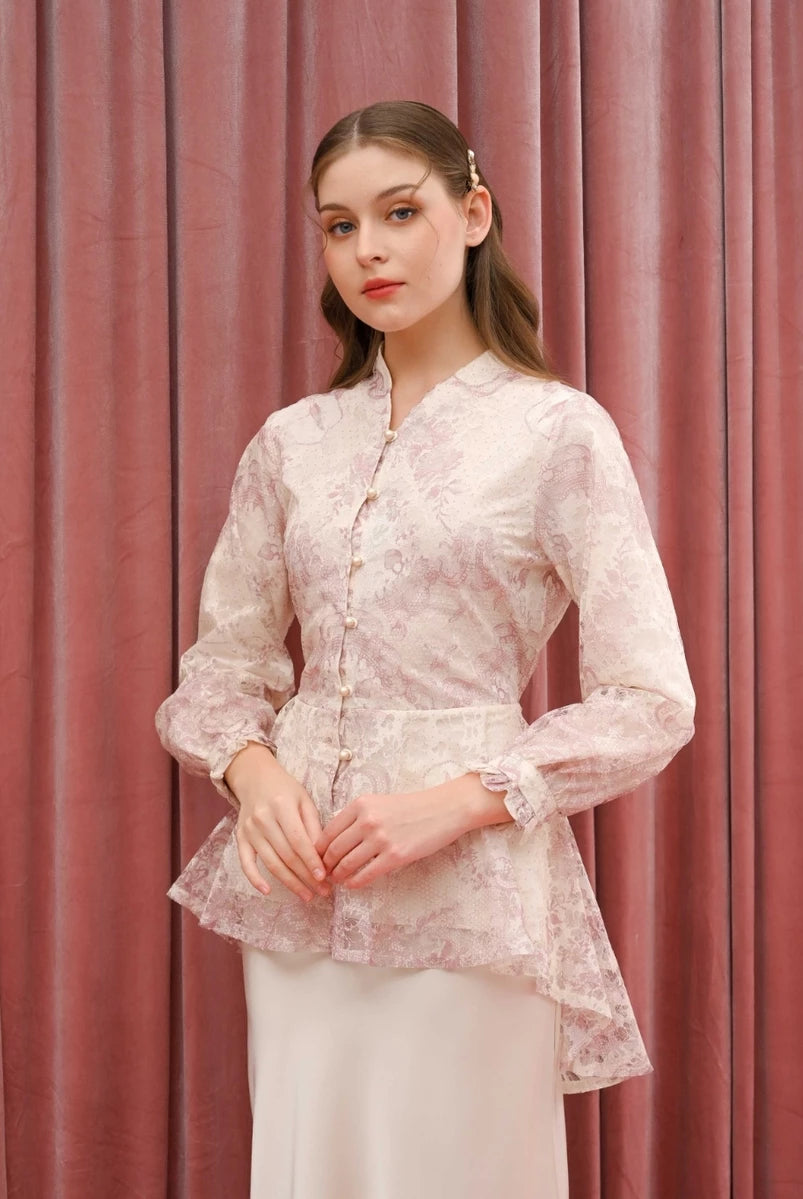 Woman wearing a light pink floral blouse by Kasa Heritage and white pants against a pink curtain background