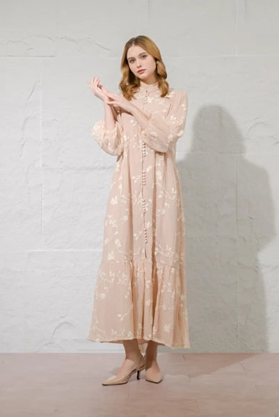 Woman wearing a long, light-colored dress with floral patterns by Kasa Heritage against a plain background