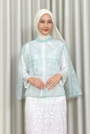 Woman wearing a light blue embroidered vest by Kartinis Label and white skirt against a plain background