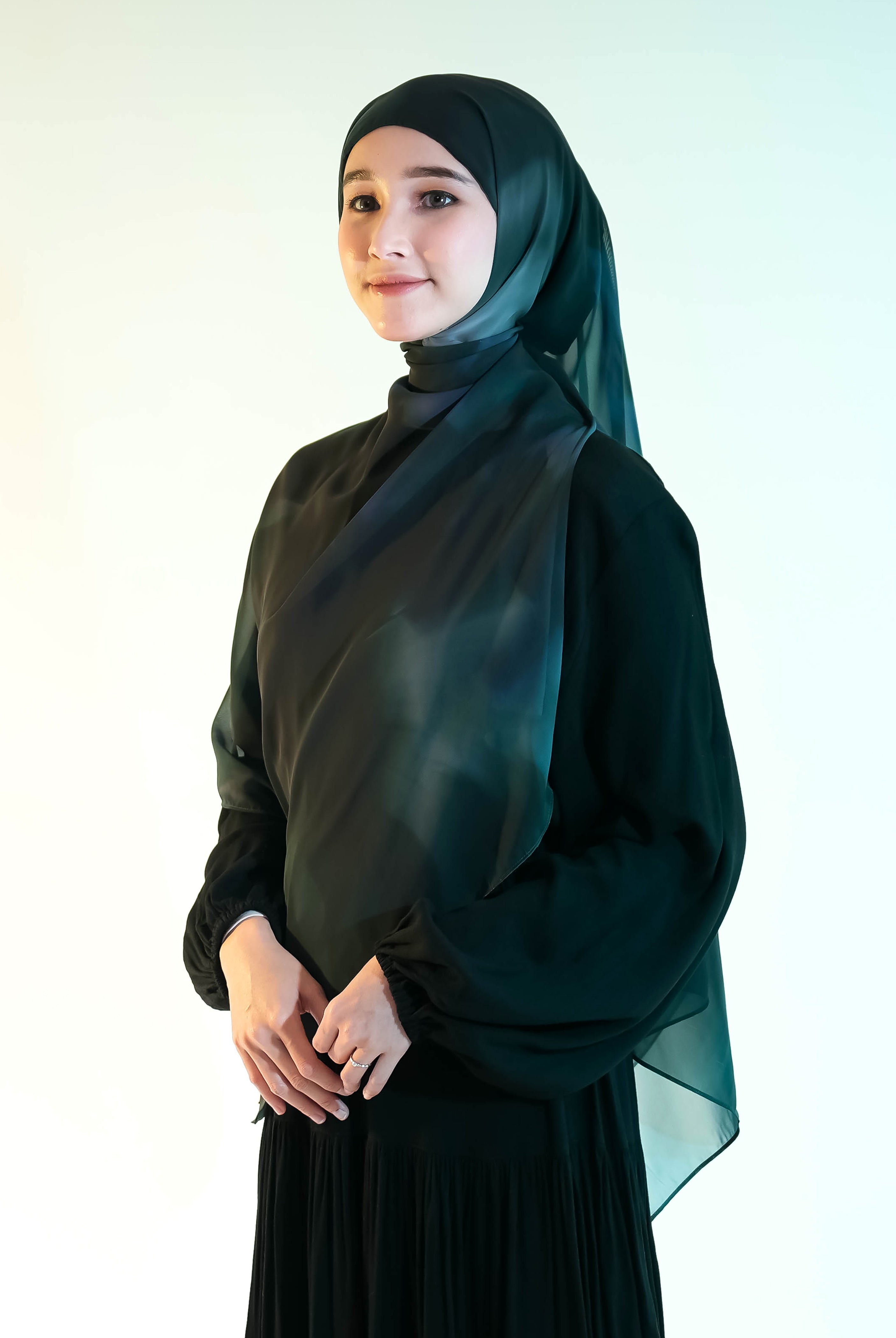 Woman wearing a dark green pashmina hijab by Puru Kambera and dress against a white background