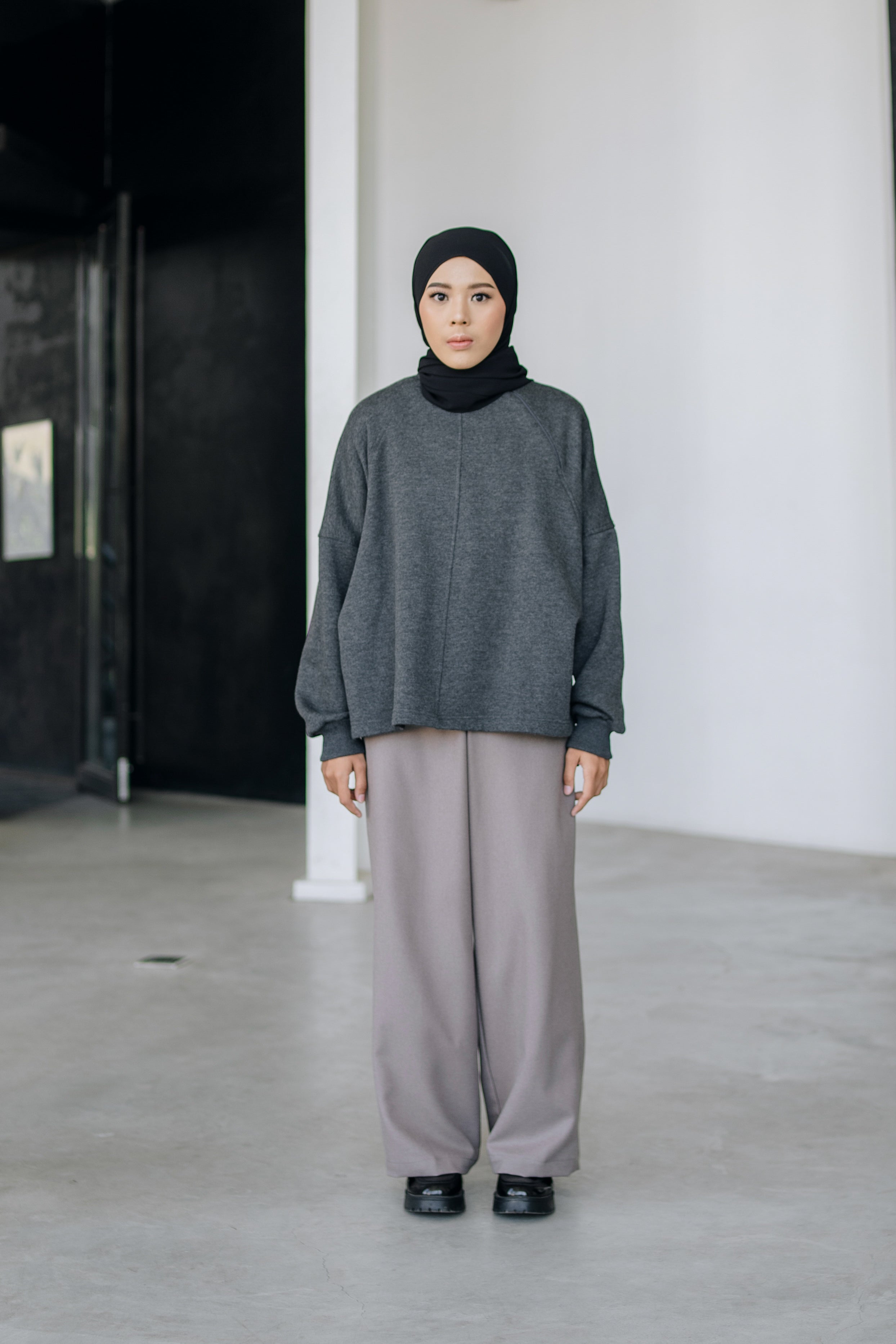 A person wearing an oversized sweater in dark grey color by Swifter, paired with a long skirt.