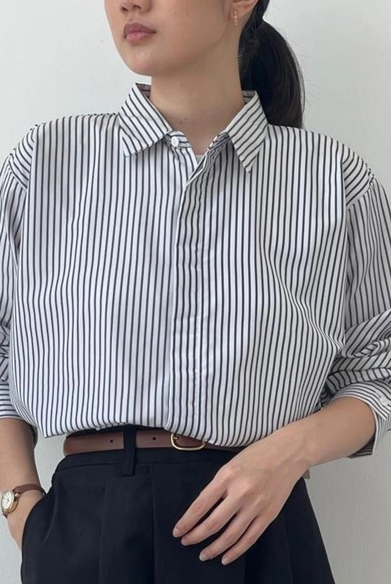 A person wearing a striped button-up shirt from BWBYAZ in black and white, with the shirt's collar visible and a watch on the left wrist.