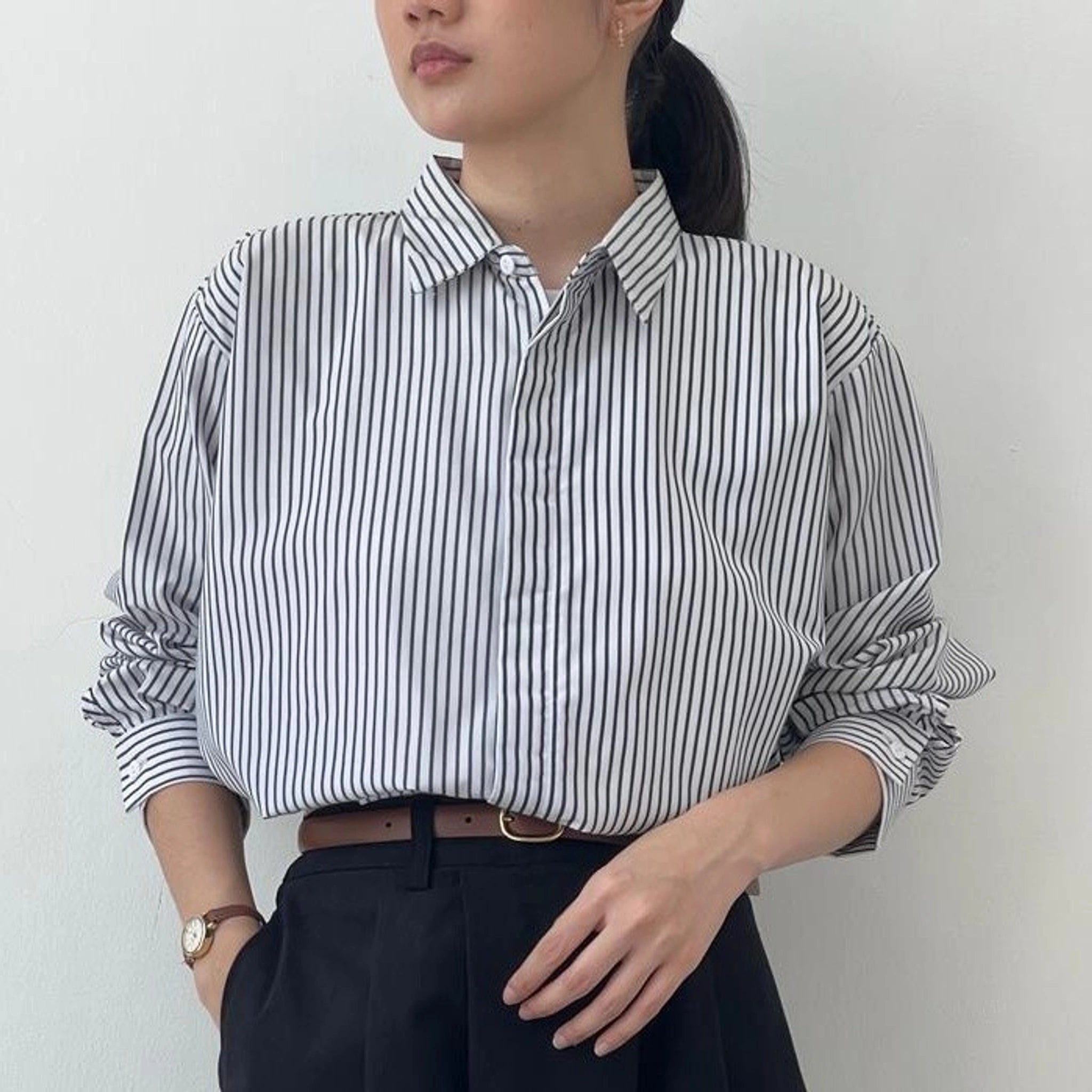 A person wearing a striped button-up shirt from BWBYAZ in black and white, with the shirt's collar visible and a watch on the left wrist.