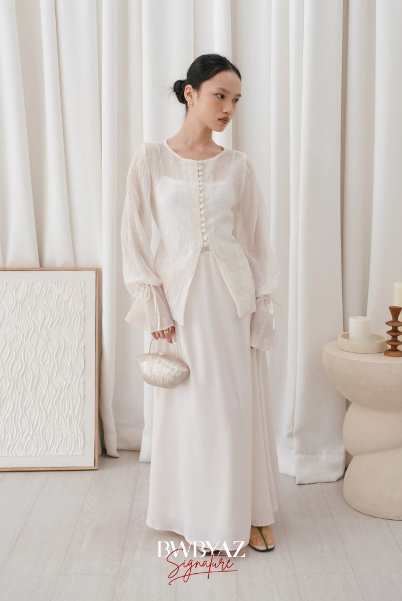 A woman wearing a white, long-sleeved blouse with front buttons and a waist tie from BWBYAZ, paired with a white skirt.