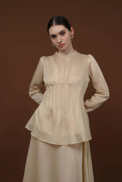 Woman wearing a beige long-sleeve soft lyocell top designed with pleats, a fitted waist, and puffy shoulders.