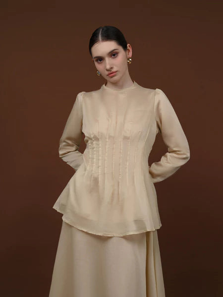 Woman wearing a beige long-sleeve soft lyocell top designed with pleats, a fitted waist, and puffy shoulders.