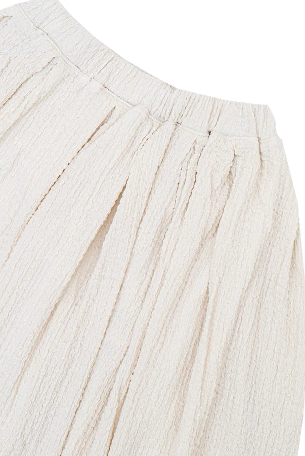 Close-up of a textured cream-colored textured balloon skirt by Yestoday, showing the pleated waistband and fine woven texture against a white background.