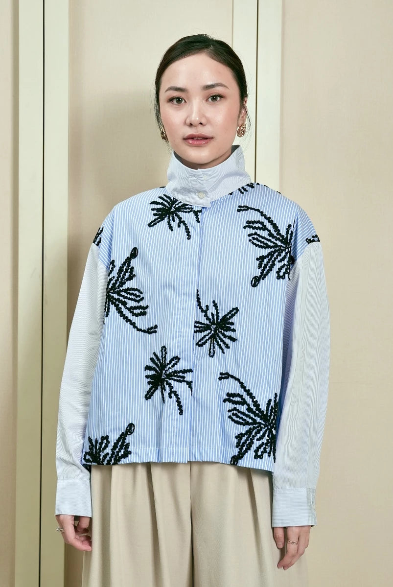 Woman wearing a light blue striped shirt by Studio Tui with black floral patterns against a neutral background
