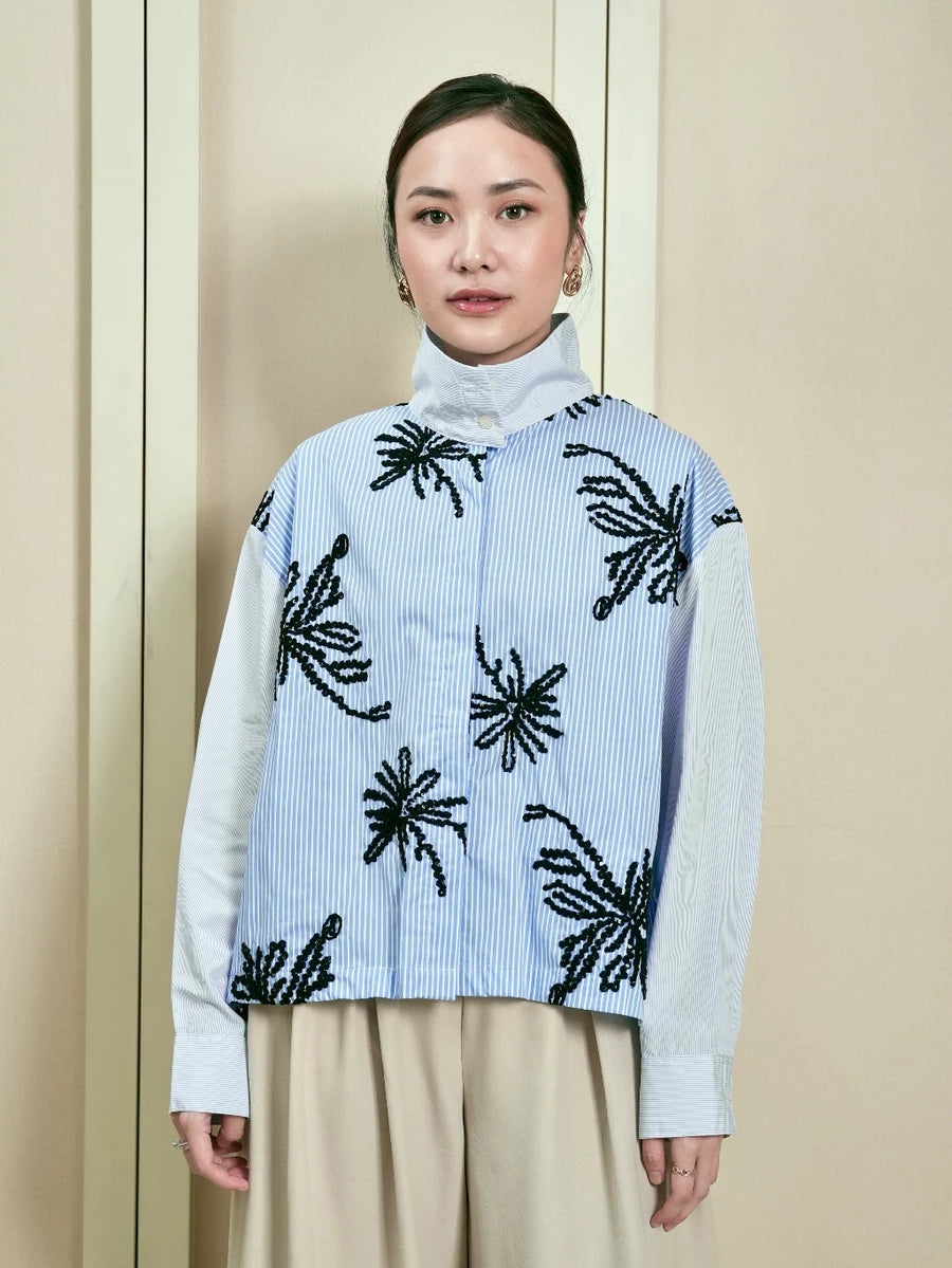 Woman wearing a light blue striped shirt by Studio Tui with black floral patterns against a neutral background