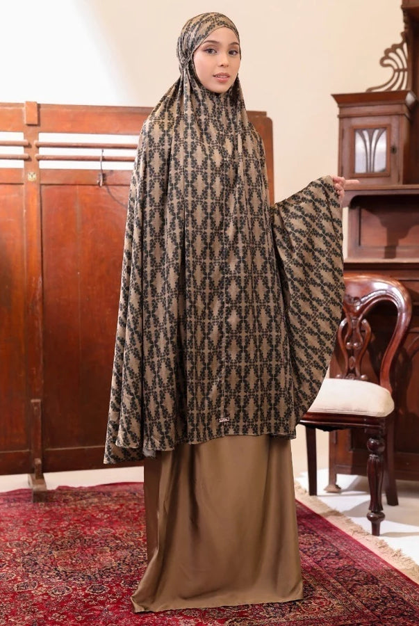 Woman wearing a patterned olive-colored prayer set by Lozy Hijab in an indoor setting with wooden furniture.