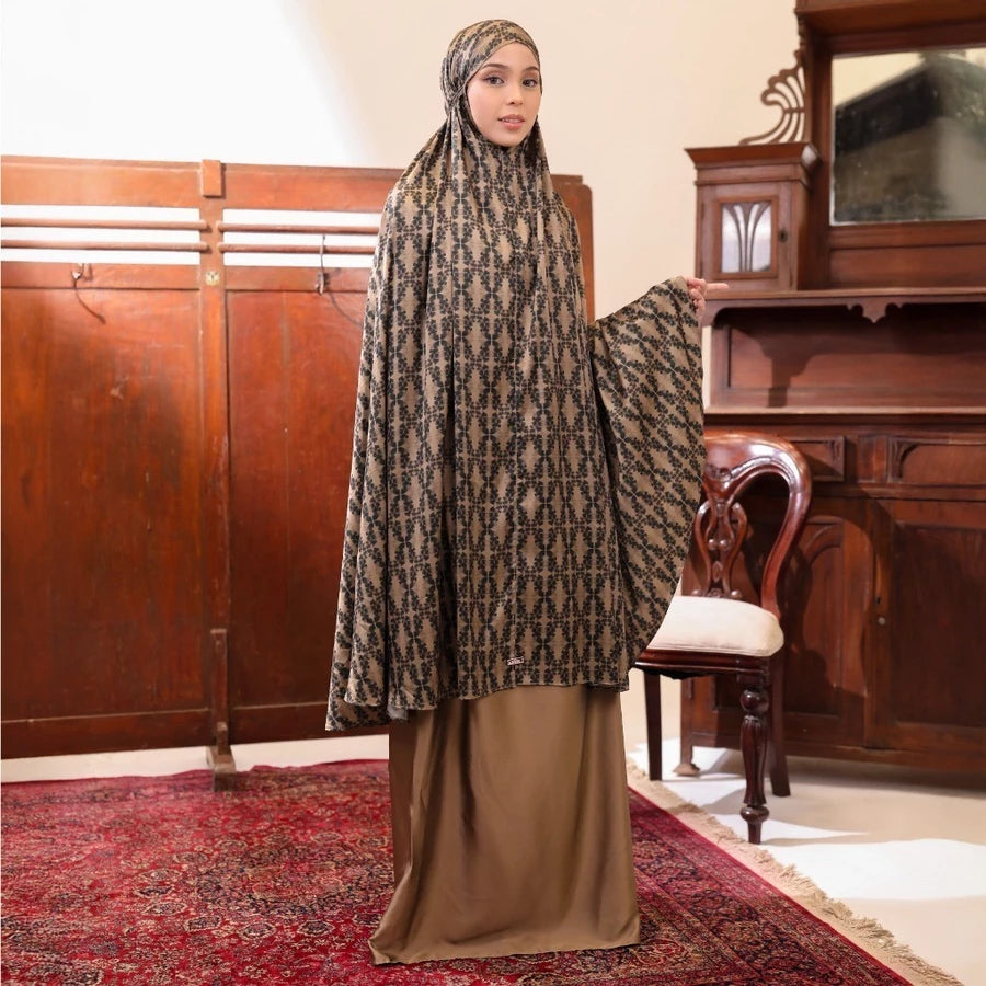 Woman wearing a patterned olive-colored prayer set by Lozy Hijab in an indoor setting with wooden furniture.
