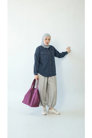Person wearing a hijab and blue denim shirt by Abame, holding a purple bag against a white background