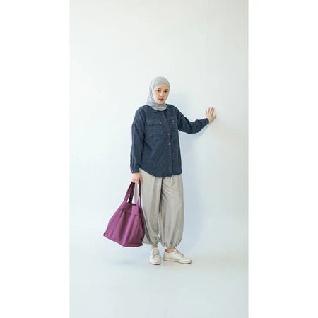 Person wearing a hijab and blue denim shirt by Abame, holding a purple bag against a white background