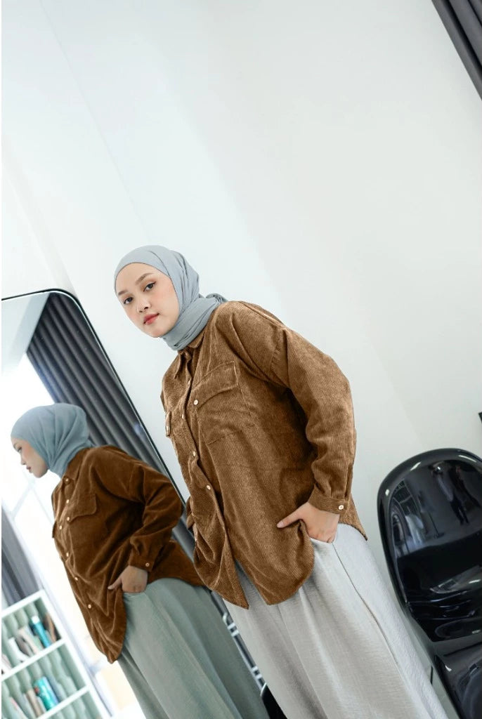 Woman wearing a brown shirt by Abame and gray hijab standing in front of a mirror.
