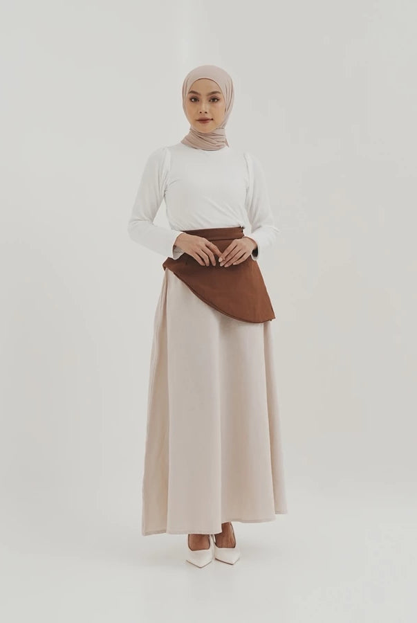 Woman wearing a white top and beige skirt by Tunique with a brown accents on a white background