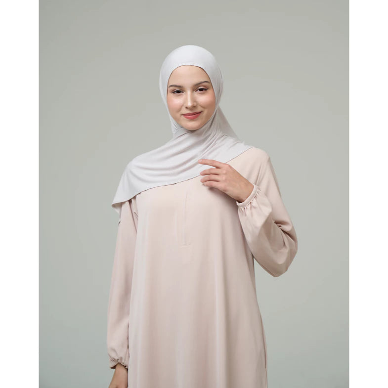 Woman wearing a light grey hijab by Inanna and dress against a gray background