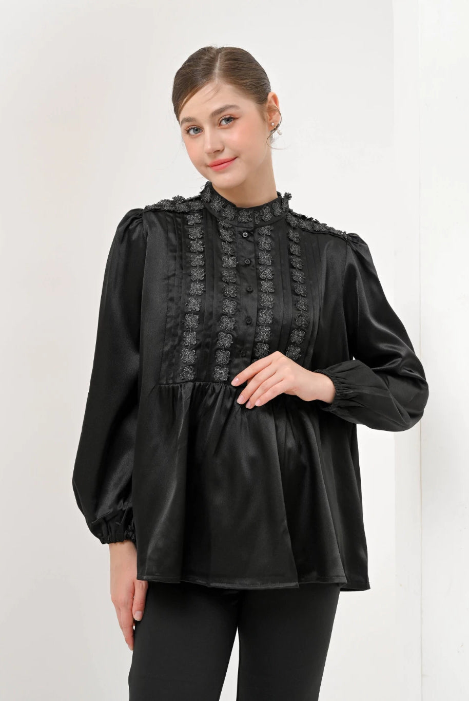 A woman wearing a black Valca Blouse by Kasa Heritage with long sleeves and a round neckline, made of silk, with a visible textured pattern.