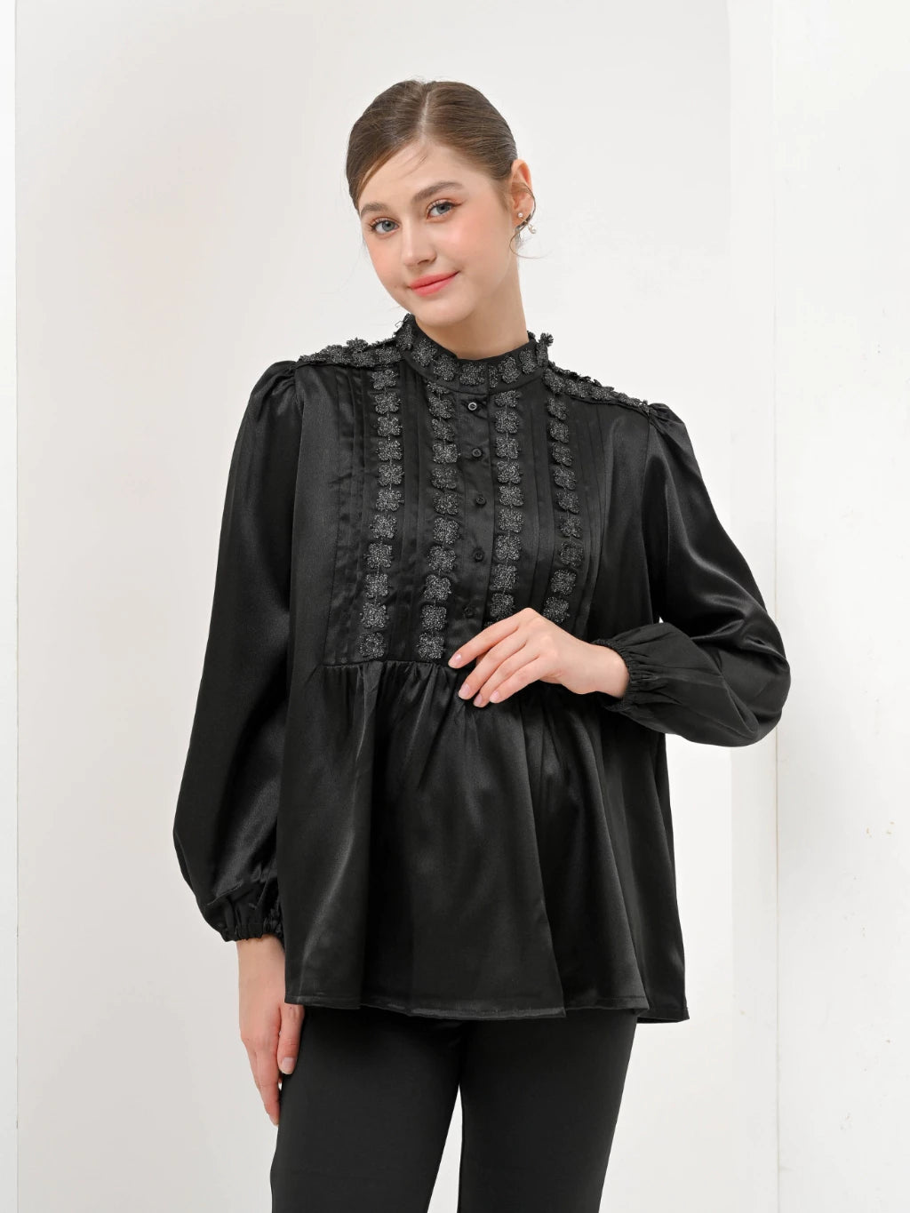 A woman wearing a black Valca Blouse by Kasa Heritage with long sleeves and a round neckline, made of silk, with a visible textured pattern.