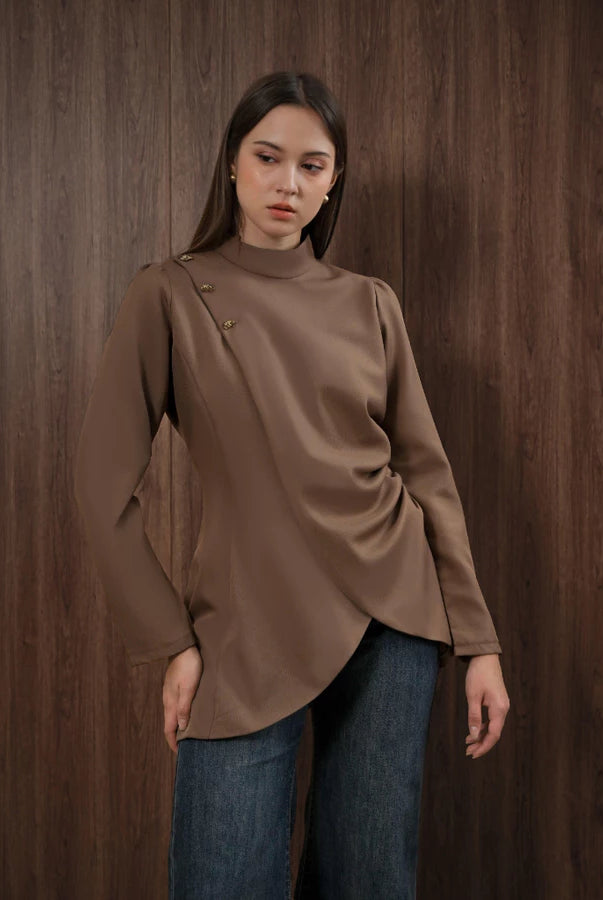 Woman wearing a brown blouse and blue jeans by Kasa Heritage against a wooden background