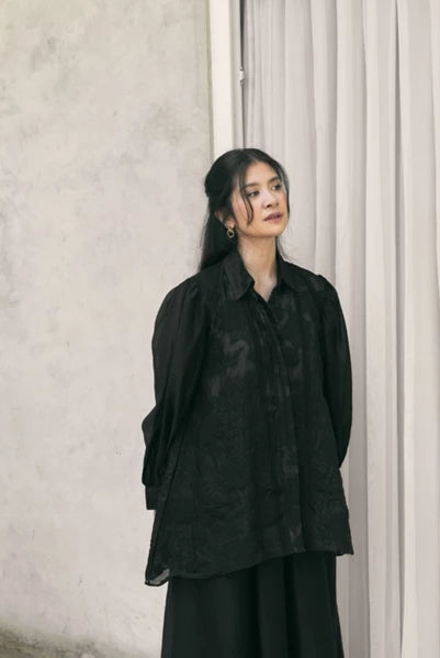 Woman wearing a black shirt by Studio Tui standing against a neutral wall.
