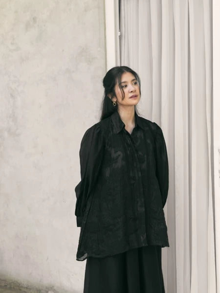 Woman wearing a black shirt by Studio Tui standing against a neutral wall.