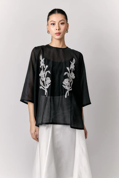 Woman wearing a black sheer blouse by Studio Tui with floral embroidery on a plain background