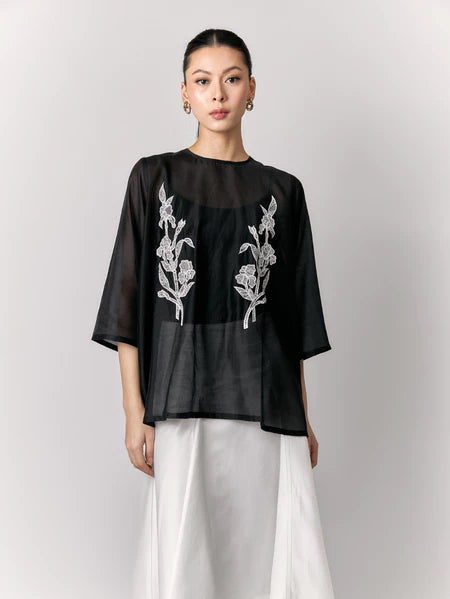 Woman wearing a black sheer blouse by Studio Tui with floral embroidery on a plain background
