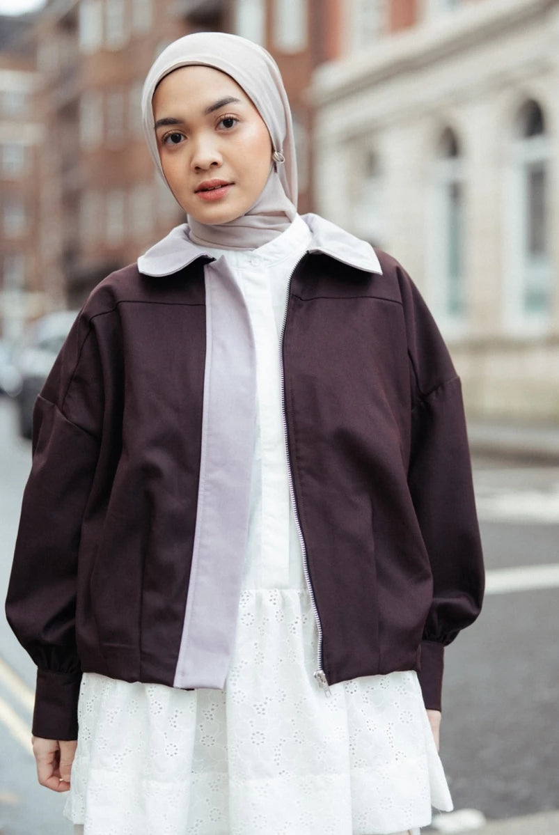Woman wearing a brown jacket by Haidee Orlin over a white shirt and skirt on a city street.