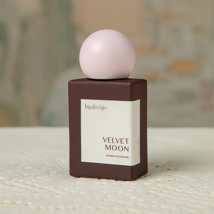 Perfume bottle labeled 'Velvet Moon' by hijabchic on a textured surface with a blurred background.
