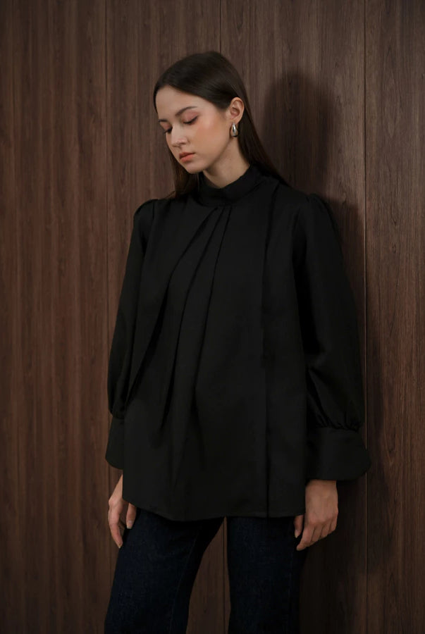 Woman wearing a black blouse by Kasa Heritage against a wooden paneled wall