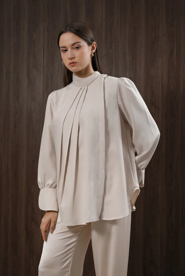 Woman wearing a beige blouse and pants by Kasa Heritage against a dark brown background