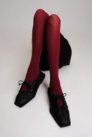 Red tights worn with black flat shoes by Cekhas on a white background