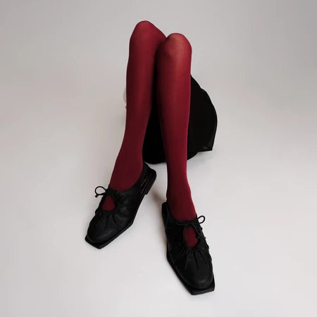 Red tights worn with black flat shoes by Cekhas on a white background