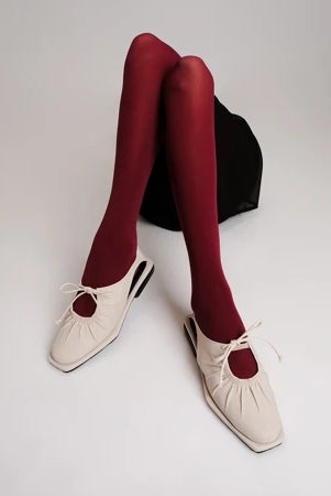 Ivory-colored flat shoes by Cekhas with red tights on a plain background