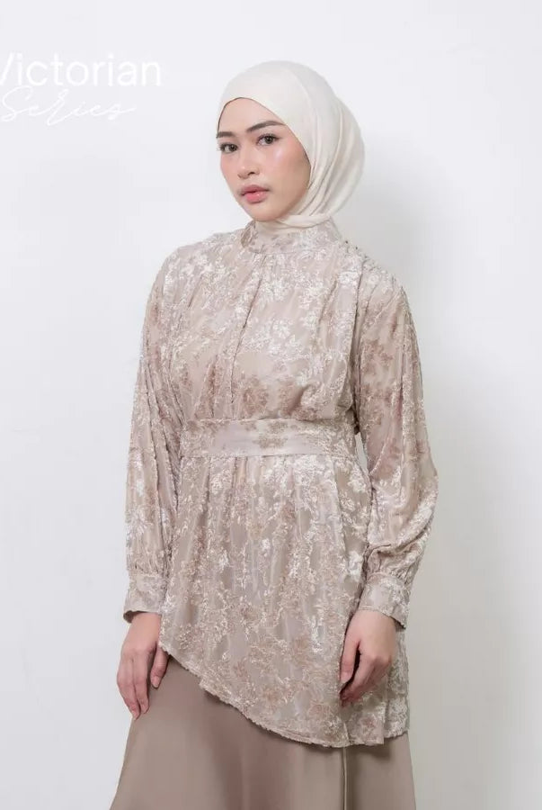 Woman wearing a beige floral lace tunic by Atala Scarves and hijab against a white background.
Seorang wanita mengenakan tunik bermotif bunga berwarna beige dengan renda dari Atala Scarves dan hijab di latar belakang putih.