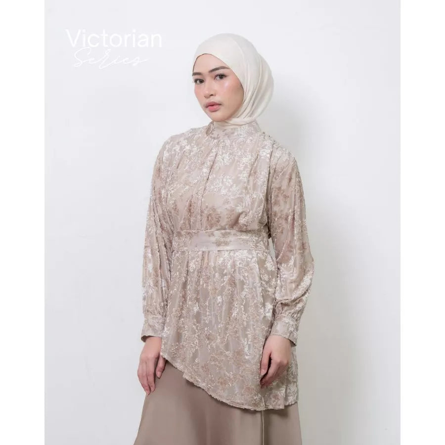 Woman wearing a beige floral lace tunic by Atala Scarves and hijab against a white background.
Seorang wanita mengenakan tunik bermotif bunga berwarna beige dengan renda dari Atala Scarves dan hijab di latar belakang putih.