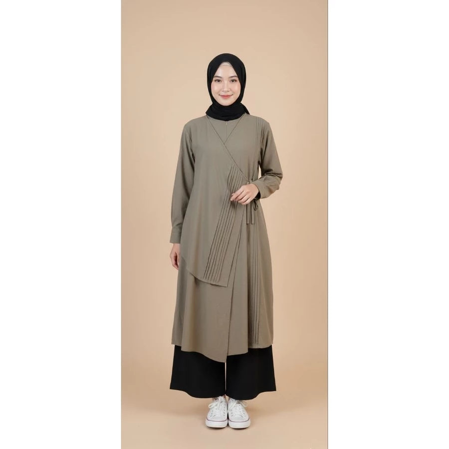 Woman wearing a long olive green tunic by Legan with a black hijab against a beige background.
Seorang wanita mengenakan tunik panjang berwarna hijau zaitun dari Legan dengan hijab hitam di latar belakang berwarna krem.